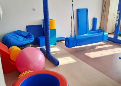 Pokój do ćwiczeń sensorycznych z huśtawkami, piłką rehabilitacyjną, materacami i siedziskami.