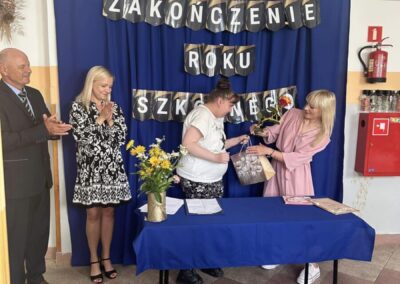 Cztery osoby na ceremonii zakończenia roku szkolnego, wręczane prezenty, kwiaty i dokumenty na stole