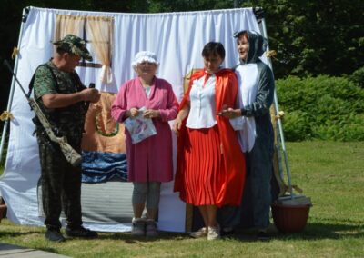 Cztery osoby w kostiumach przed dekoracją sceniczną na zewnątrz w otoczeniu zieleni.