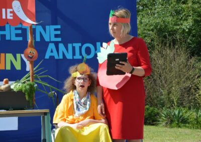 Dwie osoby z papierowymi koronami na głowach, jedna stoi z tabletem, druga na wózku inwalidzkim.