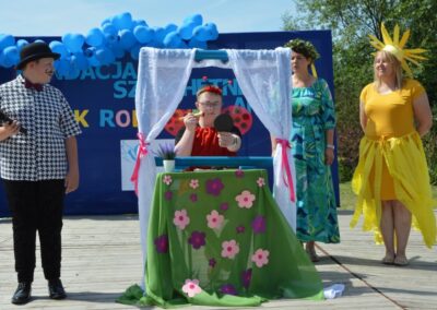 Grupa ludzi na scenie z niebieskimi balonami, jedna osoba wykonuje makijaż przed lustrem.