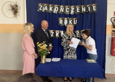 Trzy osoby przy stole z niebieskim obrusem, w tle napis "Zakończenie Roku Szkolnego".