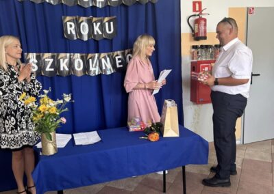 Zakończenie roku szkolnego, troje ludzi, wręczanie przedmiotów, kwiaty na stole
