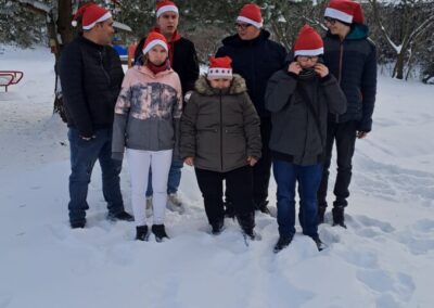 Grupa uczniów i nauczycieli w zimowych czapkach, pozująca na śniegu na tle drzew pokrytych śniegiem.