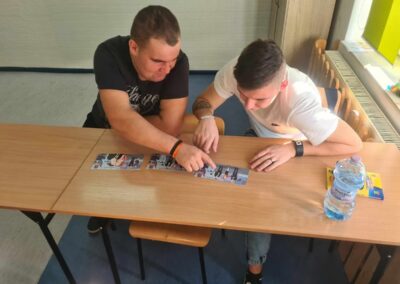 Dwóch uczniów pracujących nad zadaniem przy biurku w klasie, skoncentrowani na układaniu kart obrazkowych.