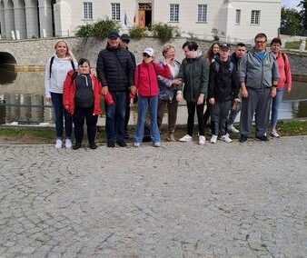 Grupa uczniów i nauczycieli podczas wycieczki do pałacu, stojąca na tle eleganckiego budynku z białą fasadą.