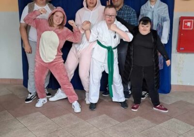 Grupa uczniów przebrana w kostiumy podczas zabawy karnawałowej, pozująca na tle niebieskiej zasłony.