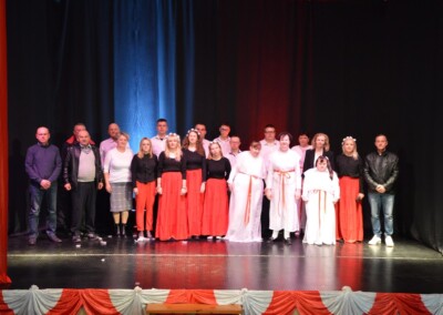 Grupa uczestników ubranych w białe i czerwone stroje, stojących na scenie podczas występu.