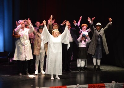 Grupa ludzi na scenie podczas przedstawienia z uniesionymi rękoma.