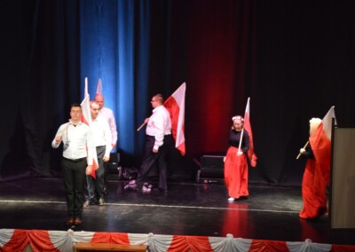 Grupa uczestników podczas występu na scenie, machających polskimi flagami.