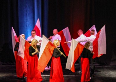 Grupa osób na scenie podczas występu, machających polskimi flagami.