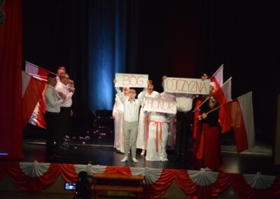 Grupa osób trzymających plakaty z napisami "Bóg, Honor, Ojczyzna" na scenie.