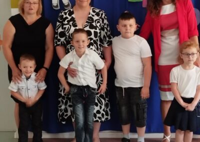 Grupa dzieci i dorosłych pozująca na tle napisu "ROKU SZKOLNEGO" z kolorową dekoracją.
