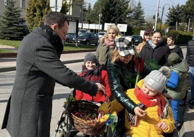 Osoby podczas marszu otrzymują słodycze z koszyka, obok kukła Marzanny. Słoneczny dzień.