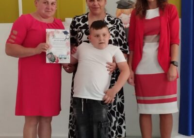 Trzy kobiety i chłopiec pozują do zdjęcia w pomieszczeniu, jedna trzyma dyplom