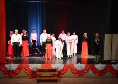 Grupa osób ustawiona w dwóch rzędach podczas występu na scenie.