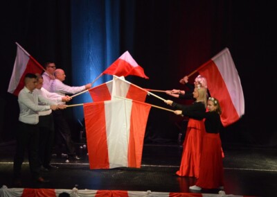 Grupa ludzi na scenie trzymająca flagi Polski w kształcie formacji przypominającej flagę narodową.