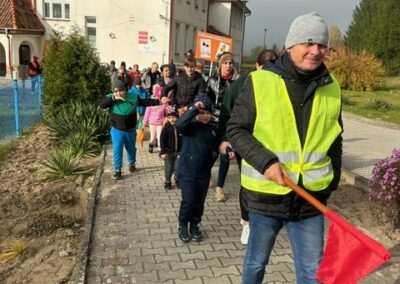 Grupa ludzi spaceruje wybrukowaną ścieżką obok budynku. Przód osoby z czerwoną flagą.