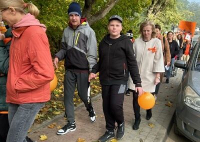 Grupa ludzi na chodniku z pomarańczowymi balonami i transparentami w jesiennym otoczeniu.