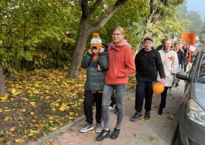 Ludzie spacerują w jesiennym parku z balonami i transparentami na chodniku.