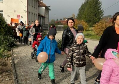 Ludzie i dzieci z pomarańczowymi balonami spacerują chodnikiem obok budynku.