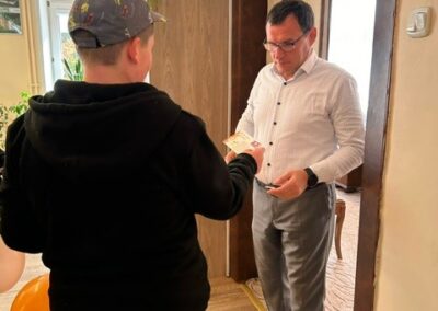Mężczyzna w białej koszuli odbiera coś od młodej osoby w czarnym ubraniu przy drzwiach.