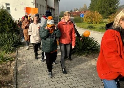 Grupa ludzi z balonami i transparentami idzie chodnikiem obok budynku w pochmurny dzień.