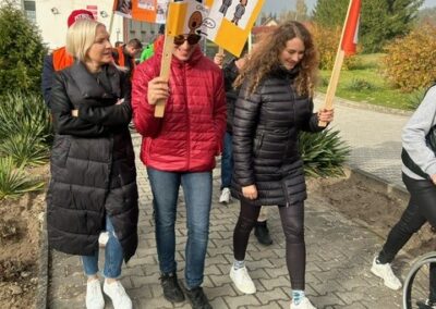 Grupa ludzi z transparentami maszerująca chodnikiem na zewnątrz.