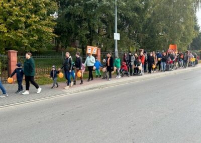 Ludzie z pomarańczowymi balonami i transparentami spacerują chodnikiem przy ulicy.