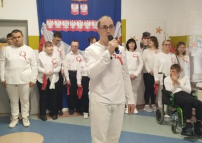 Osoby w białych ubraniach z flagami na tle godła Polski podczas obchodów 11 listopada.