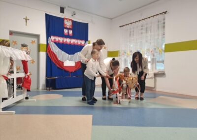 Dzieci i opiekunki bawią się w przedszkolu udekorowanym polskimi flagami i symbolami.