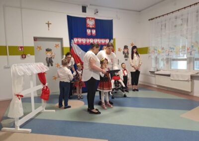 Dzieci w strojach ludowych w sali przedszkolnej z symbolami narodowymi Polski.