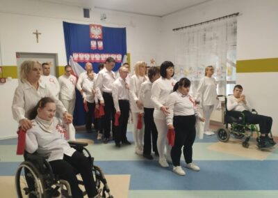 Group of people in white shirts with red accents, Polish symbols, some in wheelchairs, indoors.