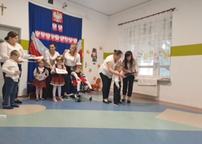Grupa osób w sali z polskimi symbolami i jesiennymi dekoracjami podczas uroczystości.