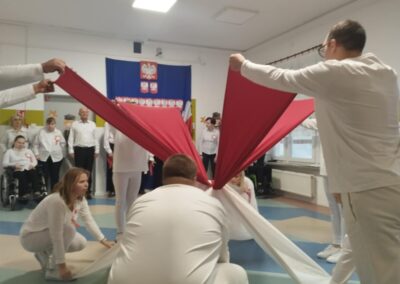Osoby w białym tworzą wzór z czerwono-białych materiałów, tło z orłem na fladze.