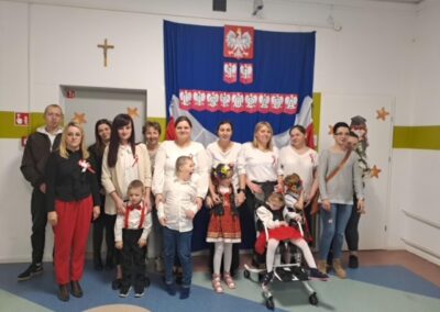 Grupa ludzi pozująca na tle biało-czerwonych dekoracji na Święto Niepodległości Polski.