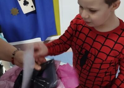 Chłopiec w stroju superbohatera otrzymuje prezent przy dekoracji z motywem kart i świecy.