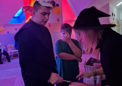 Grupa osób na imprezie tematycznej z maską i strojem czarownicy, balony i kolorowe światła.