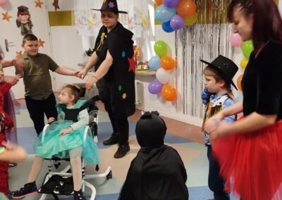 Dzieci i dorośli w kostiumach na przyjęciu z balonami i dekoracjami, dziecko na wózku.