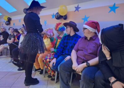 Grupa osób w kostiumach siedząca w rzędzie, z balonami i gwiezdnymi dekoracjami w tle.