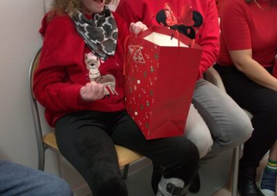 Dziecko w czapce Mikołaja i czerwonym swetrze z kobietą obok prezentu, dwie osoby ubrane na czerwono.