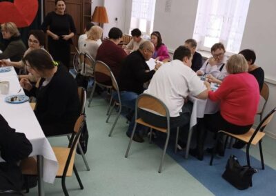 Grupa ludzi siedzi przy stołach z białymi obrusami w jasnej sali z gwiazdami na ścianach.