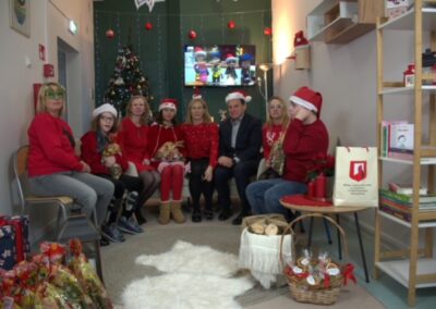 Grupa osób w stroju świątecznym z prezentami w udekorowanym pokoju z choinką.