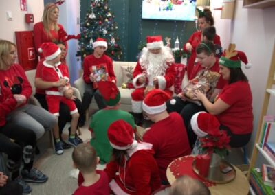 Grupa osób w czerwono-białych strojach świątecznych obok Mikołaja i choinki.