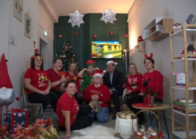 Osoby w czerwonych strojach świątecznych siedzą w dekorowanym pokoju z choinką.