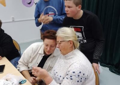 Osoby przy stole zajmują się rękodziełem, w tle kolorowe dekoracje ścienne.
