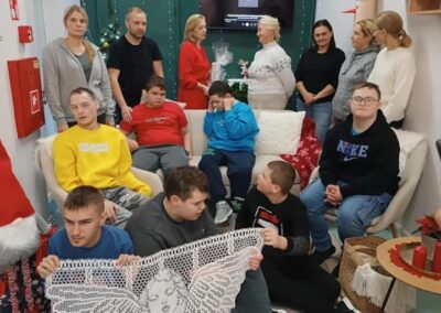 Ludzie w pokoju z dekoracjami świątecznymi, niektórzy wymieniają prezenty, koronkowy anioł na przodzie.