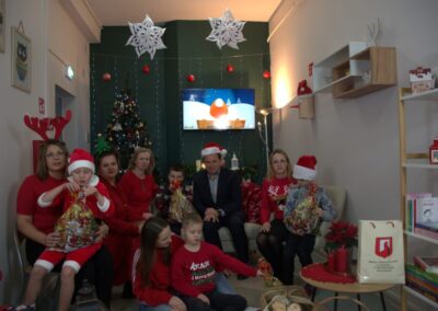 Grupa osób w świątecznych strojach, choinka, telewizor i torby z prezentami w pokoju.