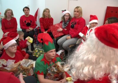 Grupa w świątecznych strojach z prezentami i dekoracjami w pokoju bożonarodzeniowym.