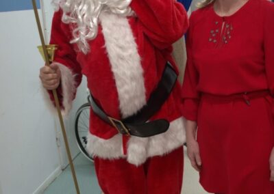 Osoba przebrana za Świętego Mikołaja i kobieta w czerwonej sukience na świątecznym tle.